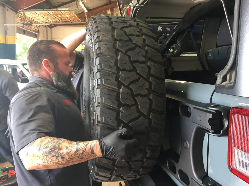 Dan at Just Jeeps in Austin placing the spare tire onto the TeraFlex tire carrier